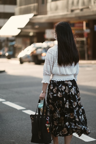 穿着白色长袖衬衫和黑色花裙子的女人白天站在人行道上